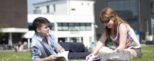 Two students sitting on the grass talking and laughing