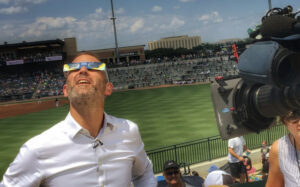 Tom Clarke wearing 3D glasses looking upwards, while filming a report