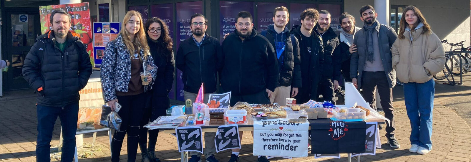 Members of the Turkish Society standing behind a table selling cakes to fundraise