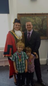 Sarah in ceremonial robes standing with her husband and two children.