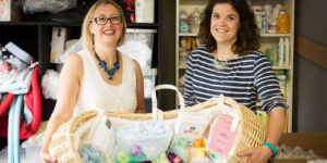 Amy and Rebecca holding a moses basket filled with baby essentials.