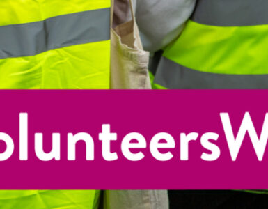 A banner reading 'Volunteers Week' with two volunteers in high-vis jackets facing away from camera