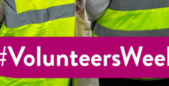 A banner reading 'Volunteers Week' with two volunteers in high-vis jackets facing away from camera