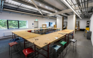 The inside of the new art building featuring long wooden desk in an L shape in a brightly lit white room.
