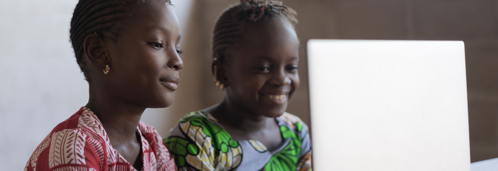 Two girls in Ghana sat in front of a laptop smiling