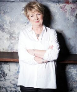 Fiona Talkington smiling to the camera wearing a white blouse, arms folded