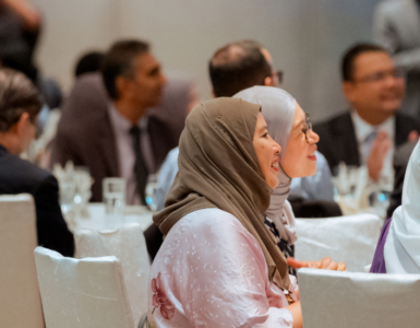 Side profile of audience smiling while sitting at tables at alumni reception, Kuala Lumpur.