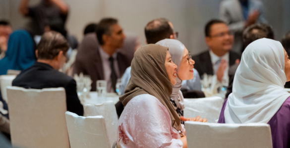 Side profile of audience smiling while sitting at tables at alumni reception, Kuala Lumpur.