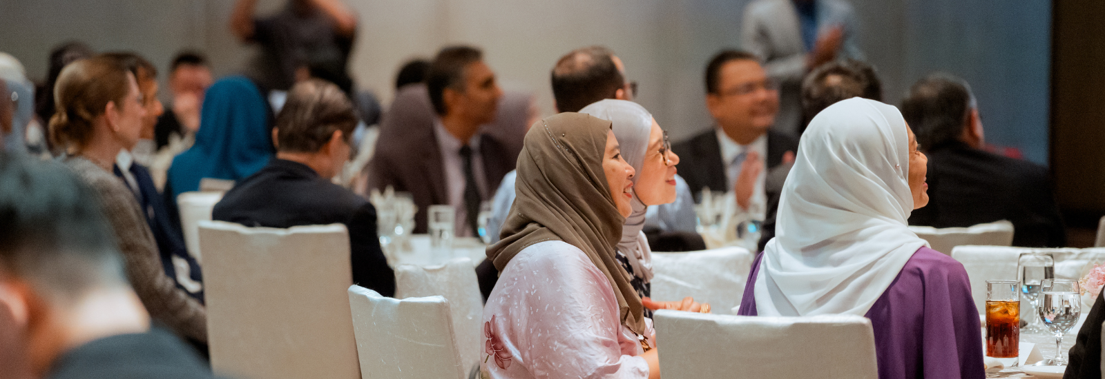 Side profile of audience smiling while sitting at tables at alumni reception, Kuala Lumpur.