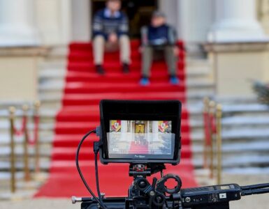 A film set showing a camera and two actors sat on steps