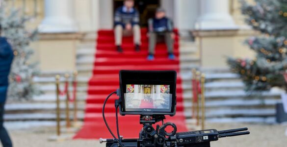 A film set showing a camera and two actors sat on steps