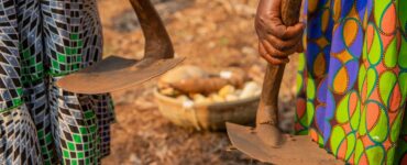 Close-up of the hands of two African women holding two hoes with a basket with the harvest of the fields,