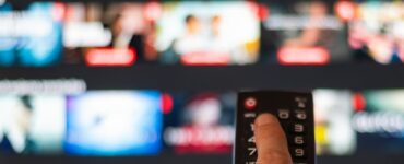 A person pressing a button on a remote with a blurred TV in the background