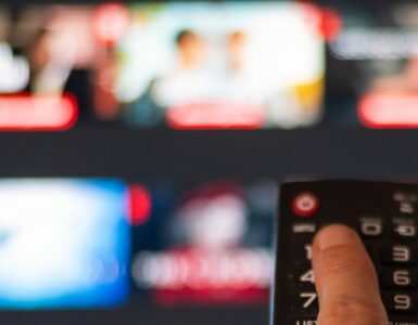 A person pressing a button on a remote with a blurred TV in the background