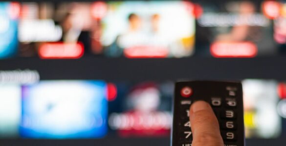 A person pressing a button on a remote with a blurred TV in the background