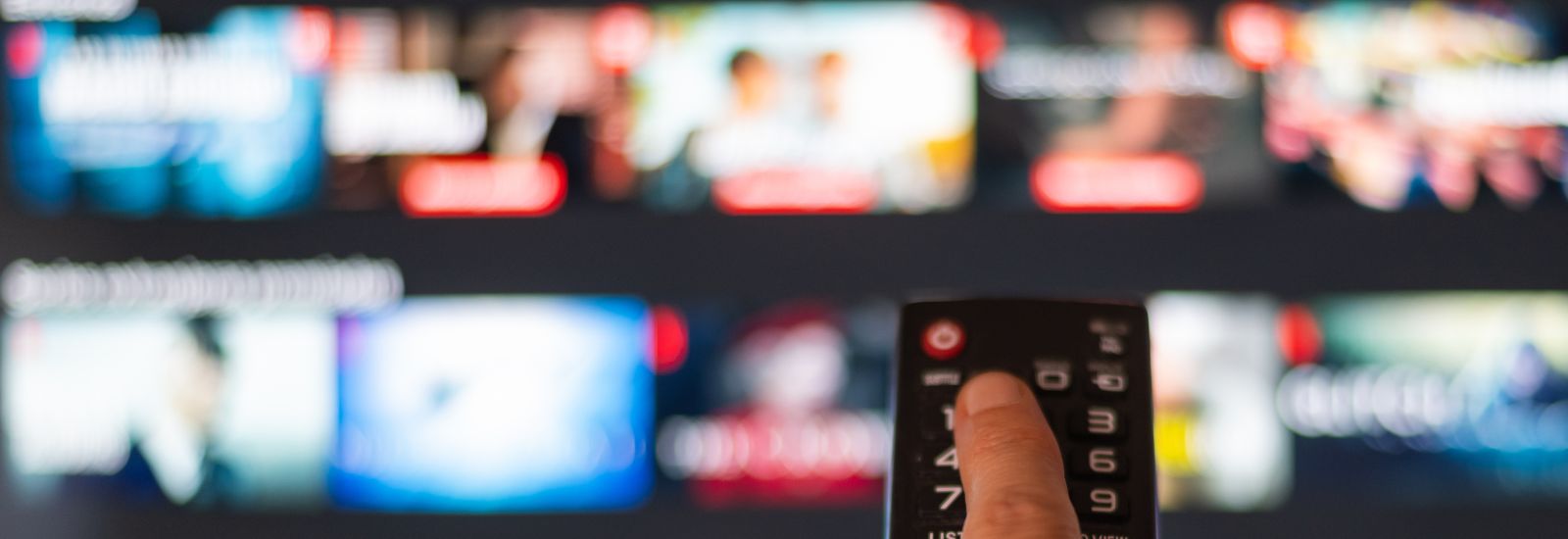 A person pressing a button on a remote with a blurred TV in the background