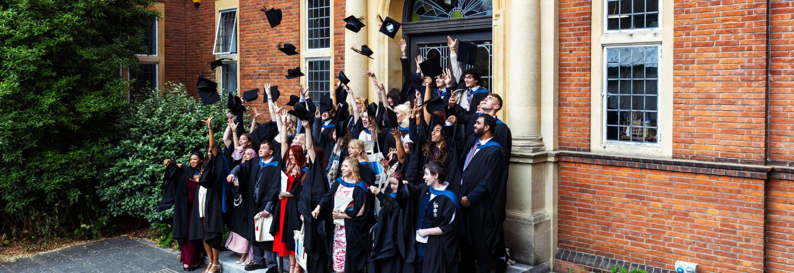 Students throwing their caps in the air at graduation on the London Road Campus steps