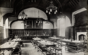The interior of Wantage Hall dining room with tables set up for dining showing the portraits of Lord and Lady Wantage hanging on the wall behind High Table