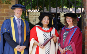 Aisha Mailk in red graduation robes stood alongside presenter Dr Sally Lloyd-Evans in red robes and Professor Peter Miskell, Presiding Officer, in blue robes.