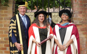 Female honorary graduate Dominique in the centre in red and white robes, stood next to Chancellor Paul Lindley in black and gold robes, and female nominator Dr Shweta Ghosh.
