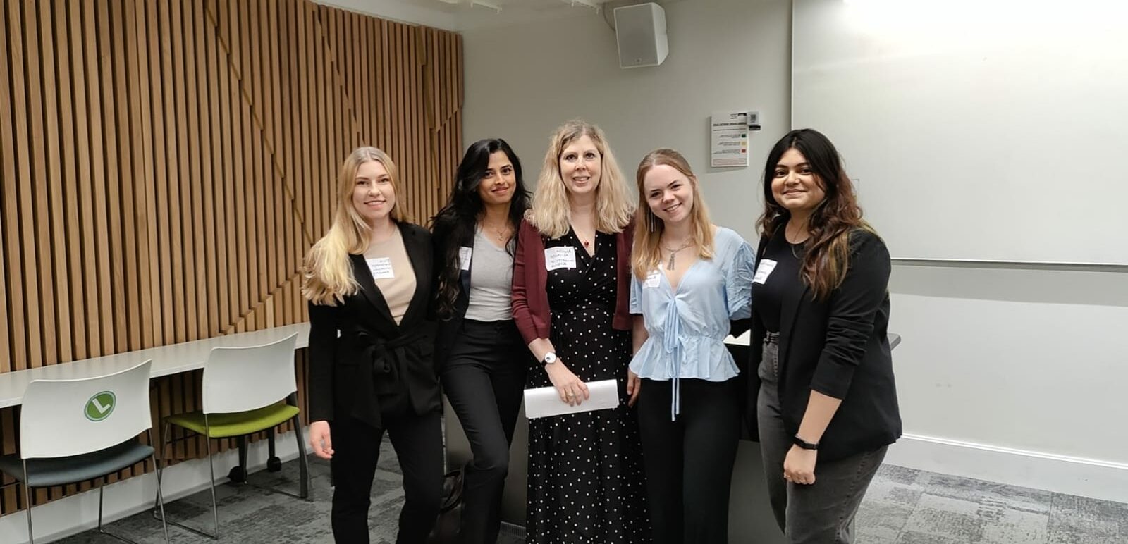 a group of women in business attire standing in front of a white and wood panelled wall