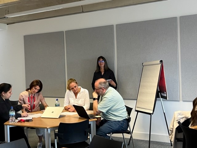 Group of people sitting around a table looking at paper and a laptop