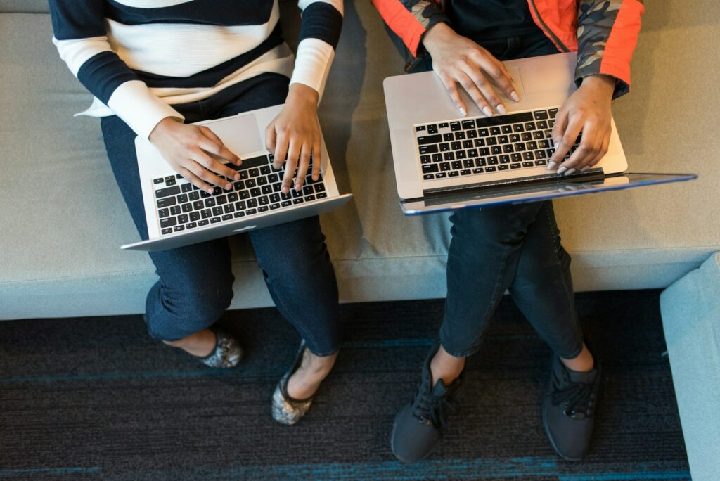 Two women using laptops sitting on a lounge