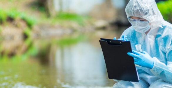 Female scientist in a white protective suit crouched in a river making notes