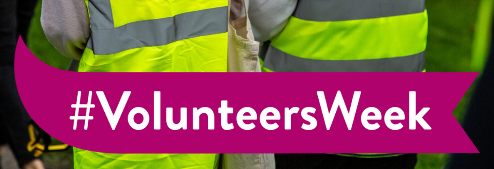 A banner reading 'Volunteers Week' with two volunteers in high-vis jackets facing away from camera