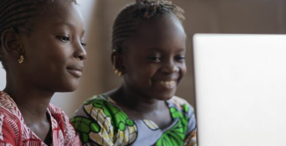 Two girls in Ghana sat in front of a laptop smiling