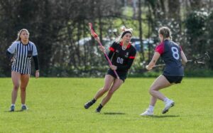 Two athletes playing lacrosse while the referee watches