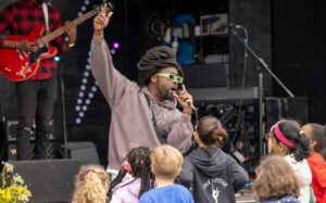 A musician singing at the Community Festival while a group of children watch