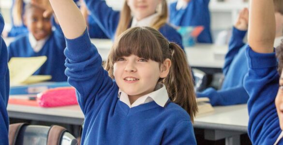 A group of school children in class with their hands raised