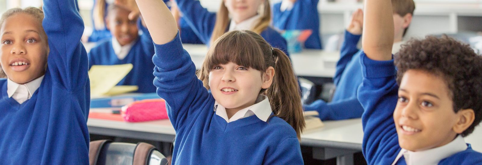 A group of school children in class with their hands raised